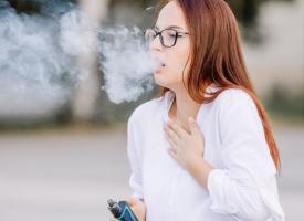 Image of young woman coughing while vaping