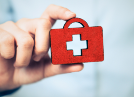 Hand holding a small symbol of a briefcase and a health cross