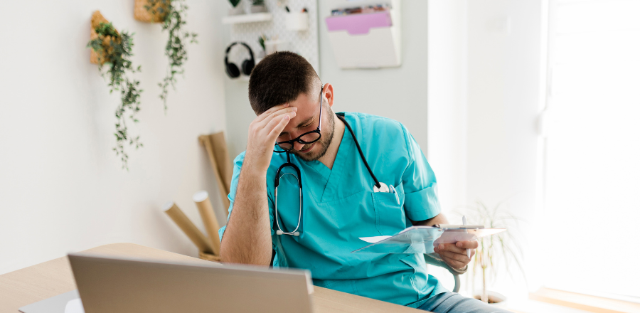 Stressed young male doctor at his desk head in hand