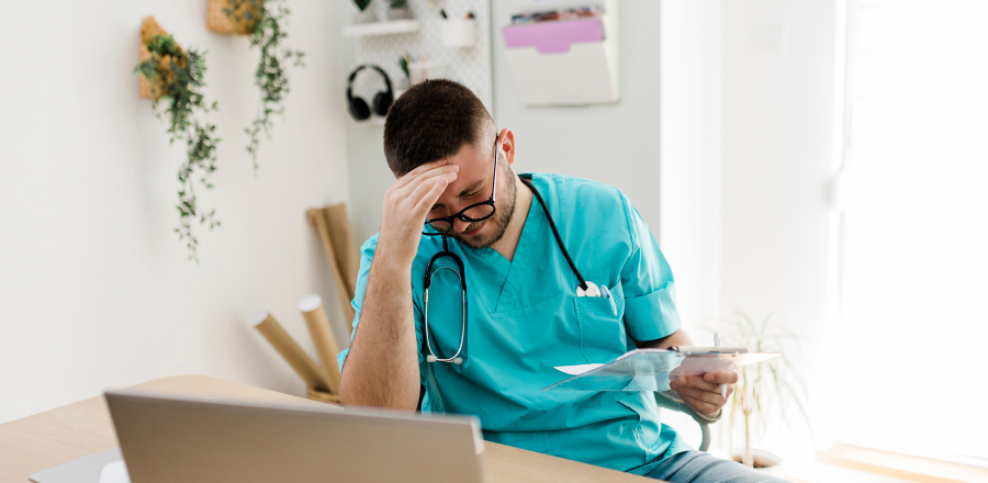 Stressed young male doctor at his desk head in hand 