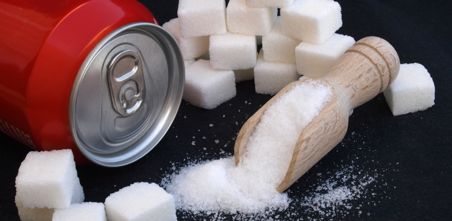 A red soft drink can lying on its side, surrounded by sugar cubes and granular sugar in a scoop